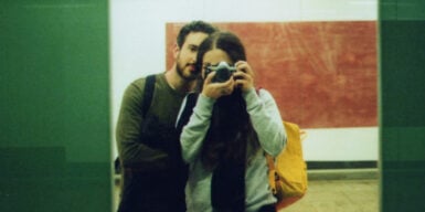 A man and a woman standing next to each other, photographing themselves in the mirror.