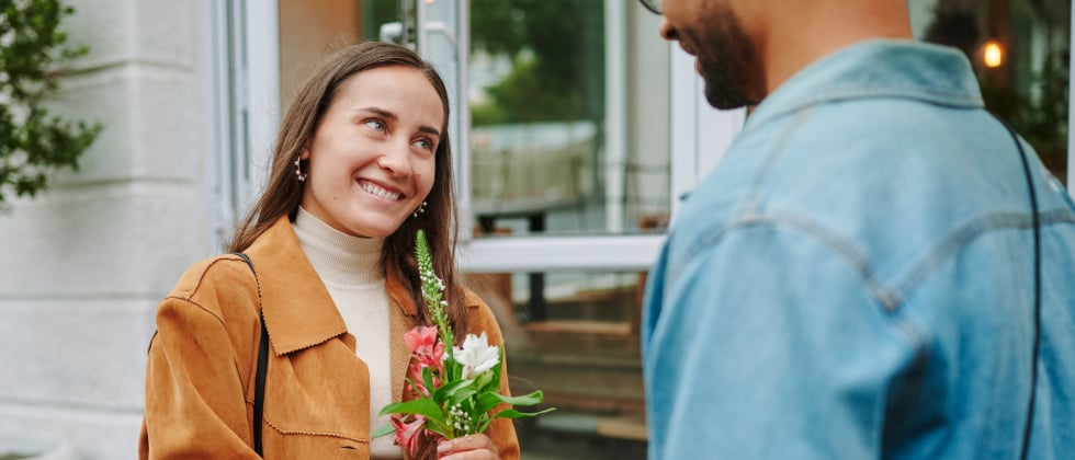 A woman smiling at a man with flowers in her hands.