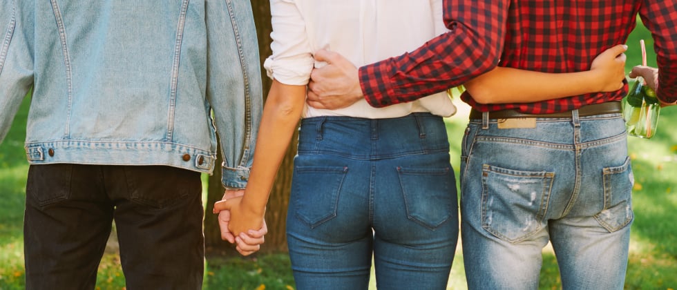 Three people from behind, two holding hands the other two hugging each other as a symbol for a polyamourious relationships