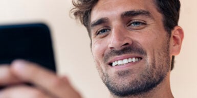 A guy smiling at his phone, thinking about how to text a girl