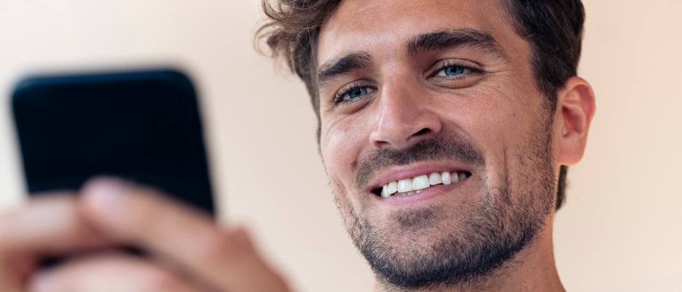 A guy smiling at his phone, thinking about how to text a girl